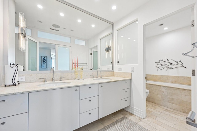 full bathroom with double vanity, a garden tub, recessed lighting, and a sink