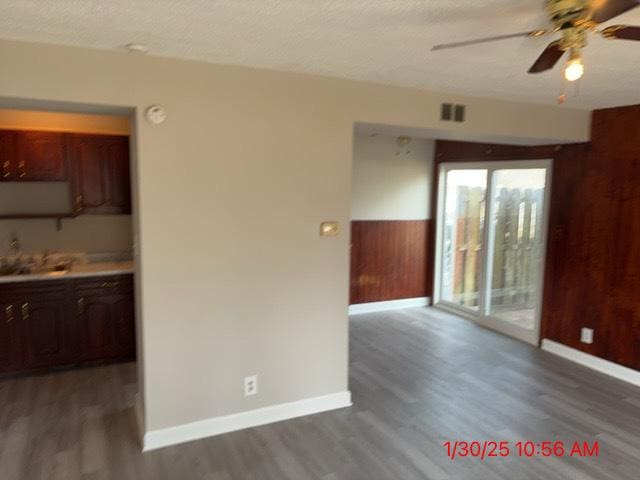 empty room with sink, a textured ceiling, wooden walls, dark hardwood / wood-style flooring, and ceiling fan