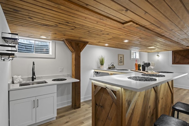 kitchen featuring a breakfast bar, sink, white cabinets, wood ceiling, and light wood-type flooring