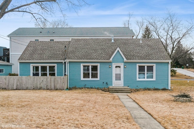 view of front of house with a shingled roof, fence, and a front lawn