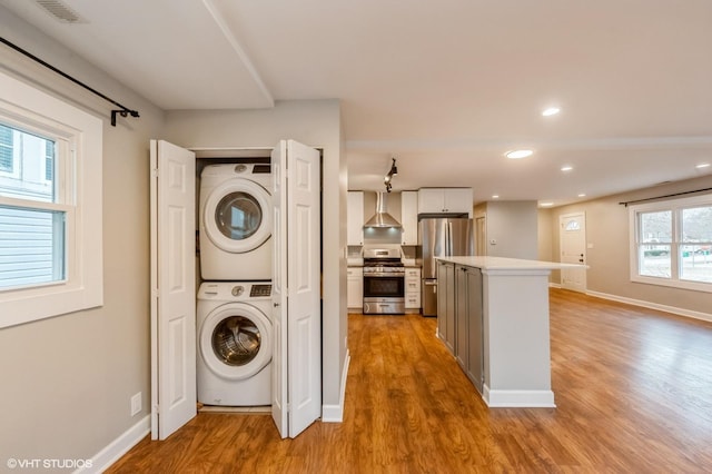 washroom with light wood-type flooring, laundry area, baseboards, and stacked washing maching and dryer