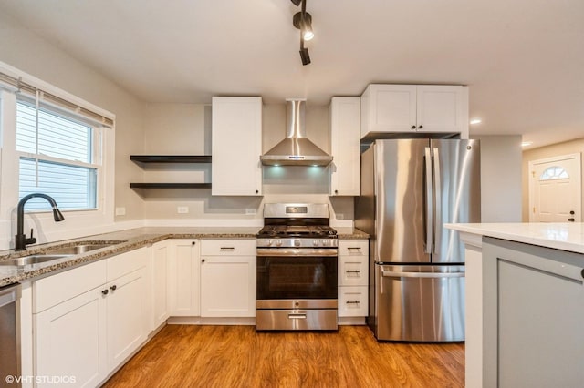 kitchen featuring wall chimney range hood, appliances with stainless steel finishes, white cabinets, and a sink