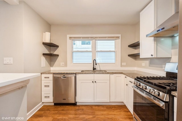 kitchen with stainless steel appliances, wall chimney range hood, white cabinetry, open shelves, and a sink