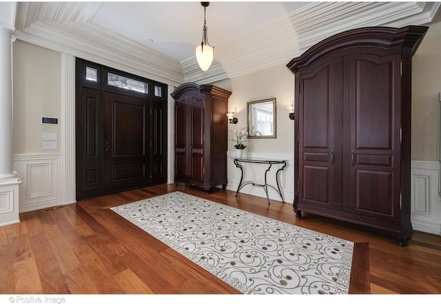 foyer entrance featuring ornamental molding, a wainscoted wall, decorative columns, and wood finished floors