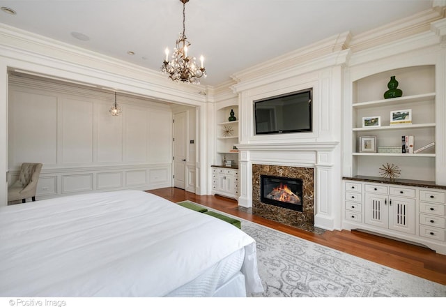 bedroom with a closet, a premium fireplace, dark wood-type flooring, a chandelier, and ornamental molding