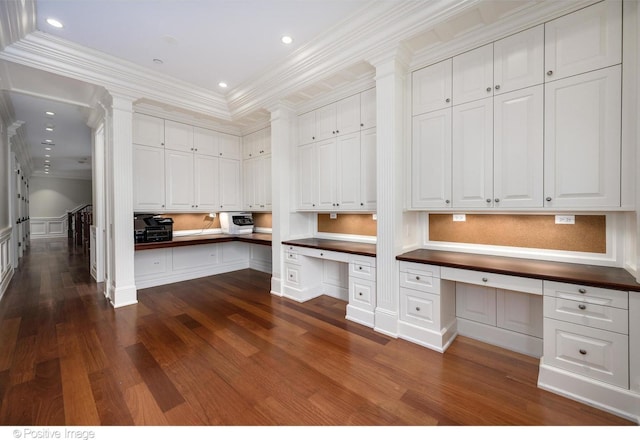 unfurnished office featuring built in desk, decorative columns, recessed lighting, dark wood finished floors, and crown molding