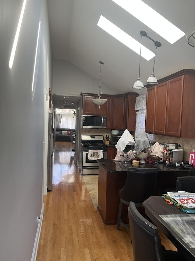 kitchen featuring vaulted ceiling with skylight, decorative light fixtures, a kitchen breakfast bar, stainless steel appliances, and light wood-type flooring