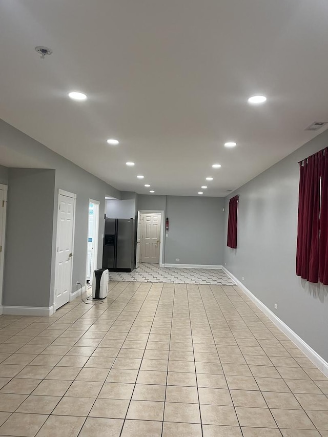 basement featuring light tile patterned floors and stainless steel refrigerator with ice dispenser