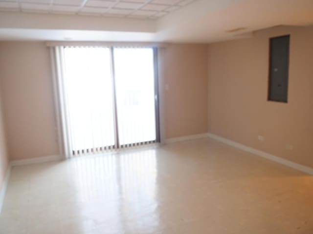 empty room with a drop ceiling, electric panel, and baseboards