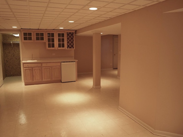 finished below grade area with indoor wet bar, a sink, a drop ceiling, and baseboards