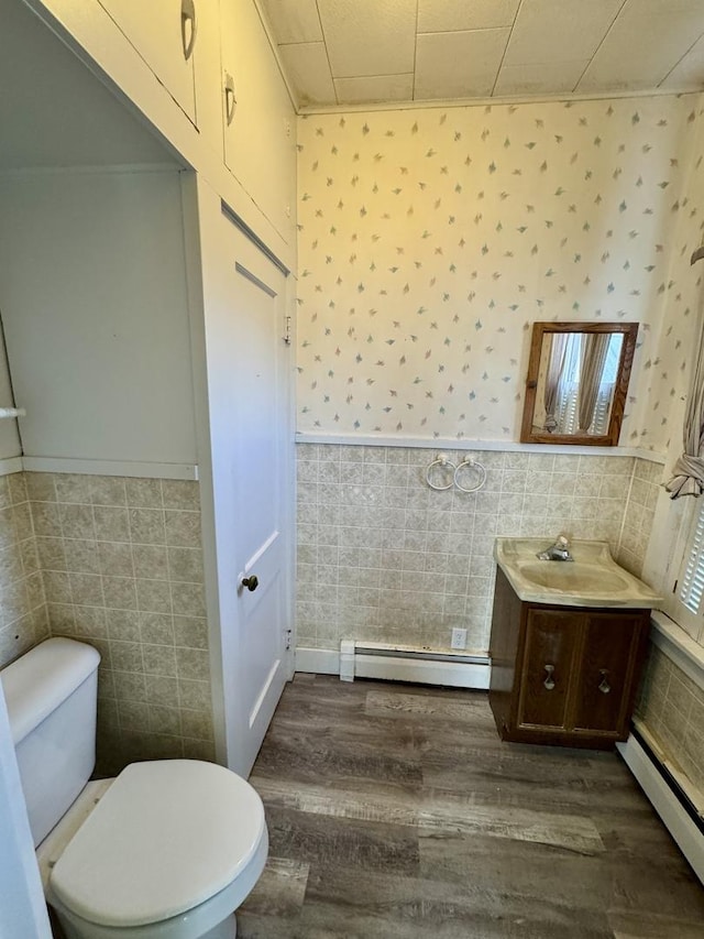 half bath featuring a baseboard heating unit, wainscoting, toilet, and wallpapered walls