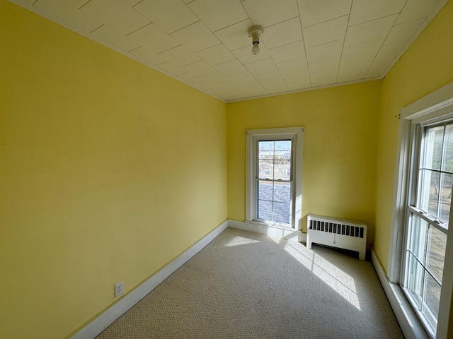 carpeted spare room with radiator, a healthy amount of sunlight, baseboards, and ornamental molding