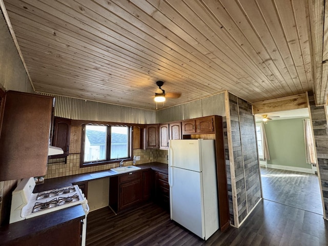 kitchen with a sink, range with gas stovetop, freestanding refrigerator, dark countertops, and dark wood finished floors