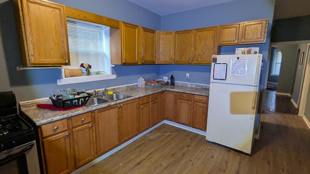 kitchen featuring wood-type flooring, gas range oven, sink, and white fridge