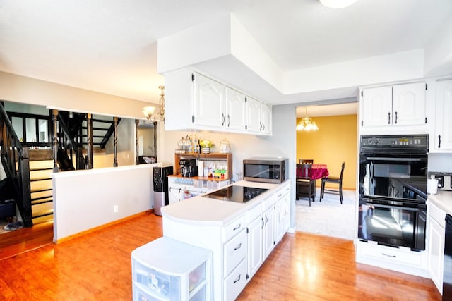 kitchen with light wood-type flooring, black appliances, white cabinets, and an inviting chandelier