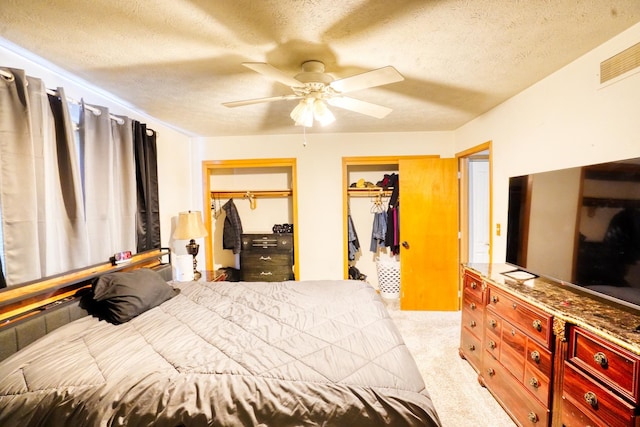 bedroom with light carpet, a textured ceiling, visible vents, and multiple closets