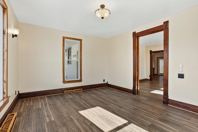 empty room with dark wood-style floors, baseboard heating, visible vents, and baseboards