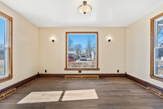 empty room with dark wood-type flooring, visible vents, and baseboards