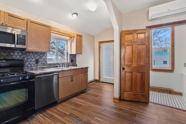 kitchen featuring dark countertops, dark wood-style floors, a wall unit AC, stainless steel appliances, and a sink