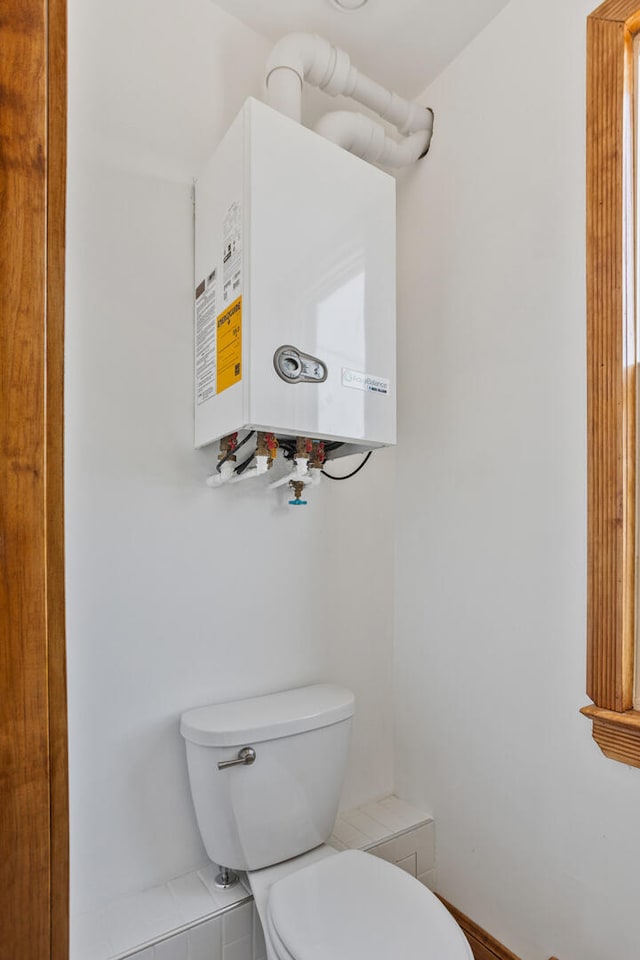 half bath featuring tankless water heater, baseboards, and toilet