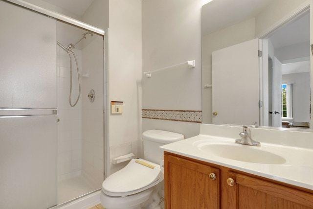 bathroom featuring vanity, a shower with door, and toilet