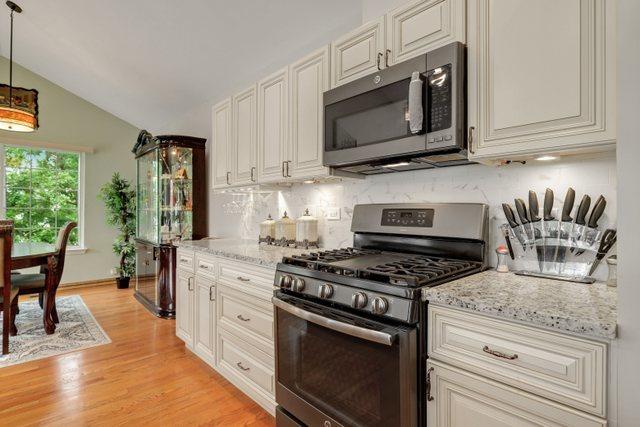 kitchen featuring vaulted ceiling, appliances with stainless steel finishes, decorative backsplash, light stone counters, and light hardwood / wood-style flooring