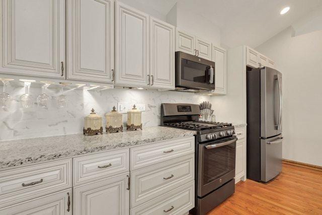 kitchen featuring decorative backsplash, stainless steel appliances, light hardwood / wood-style floors, and white cabinets