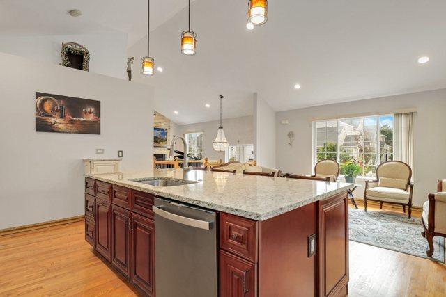 kitchen featuring stainless steel dishwasher, an island with sink, decorative light fixtures, and sink