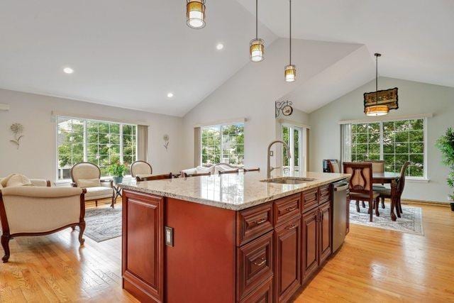 kitchen with sink, light stone counters, a center island with sink, dishwasher, and pendant lighting