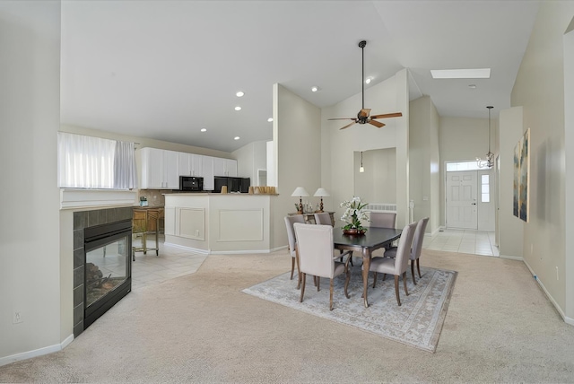 dining area featuring high vaulted ceiling, light carpet, a wealth of natural light, and a tiled fireplace