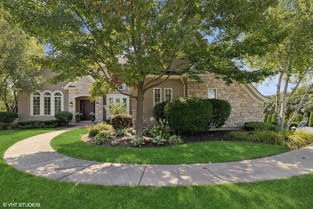 obstructed view of property with stone siding, a front lawn, and stucco siding