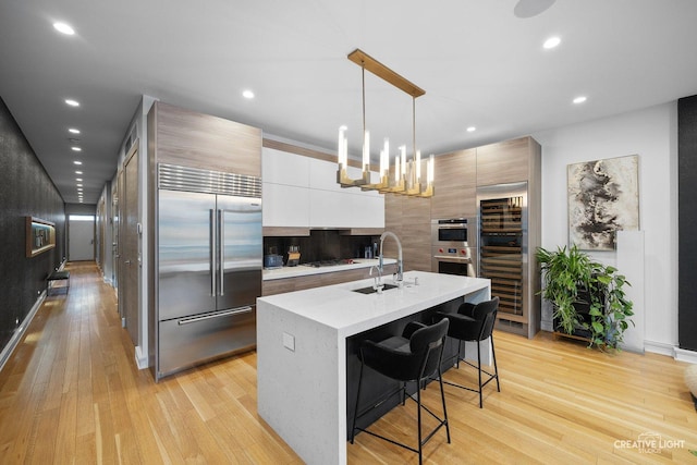 kitchen featuring appliances with stainless steel finishes, decorative light fixtures, white cabinetry, a breakfast bar area, and a kitchen island with sink