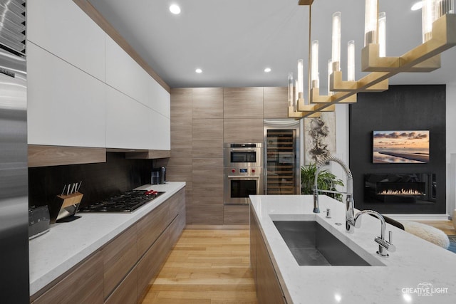 kitchen featuring sink, hanging light fixtures, stainless steel appliances, light stone counters, and white cabinets