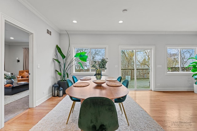 dining space featuring light wood-style floors, baseboards, visible vents, and crown molding