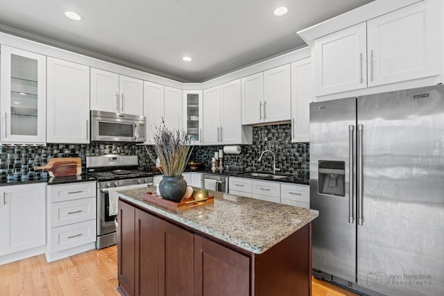 kitchen featuring light wood finished floors, tasteful backsplash, glass insert cabinets, appliances with stainless steel finishes, and a sink