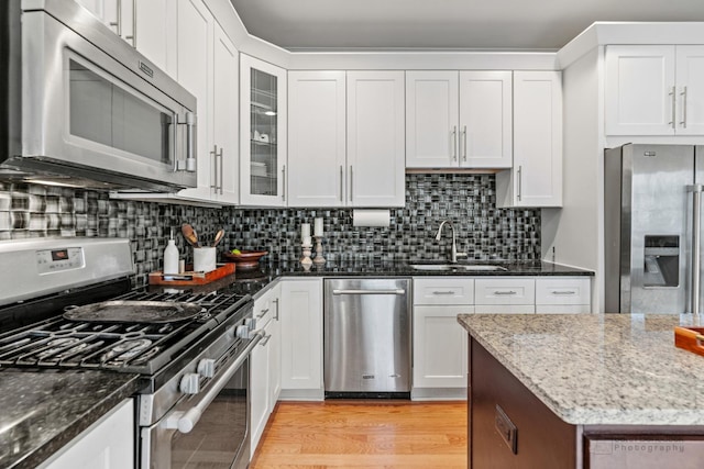 kitchen with stainless steel appliances, light wood-style flooring, decorative backsplash, a sink, and dark stone counters