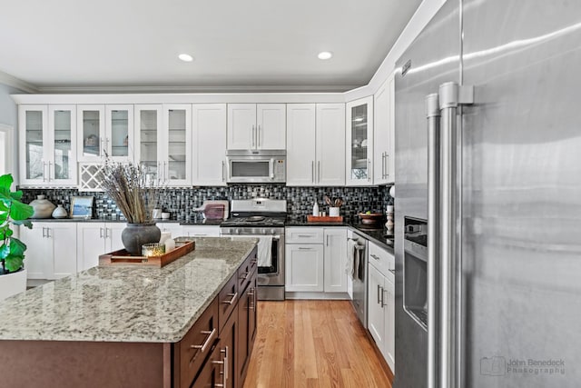 kitchen with white cabinets, light wood finished floors, stainless steel appliances, and decorative backsplash