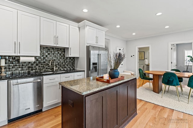 kitchen featuring crown molding, light wood finished floors, stainless steel appliances, backsplash, and a sink