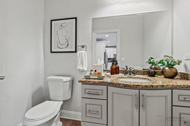 half bathroom featuring toilet, baseboards, and vanity