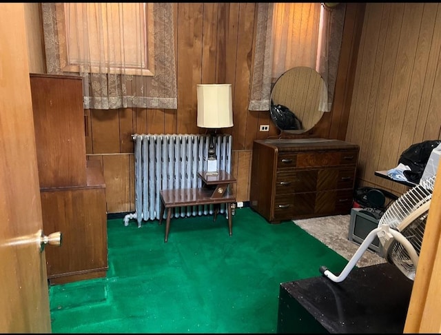 living area featuring radiator heating unit, dark carpet, and wood walls