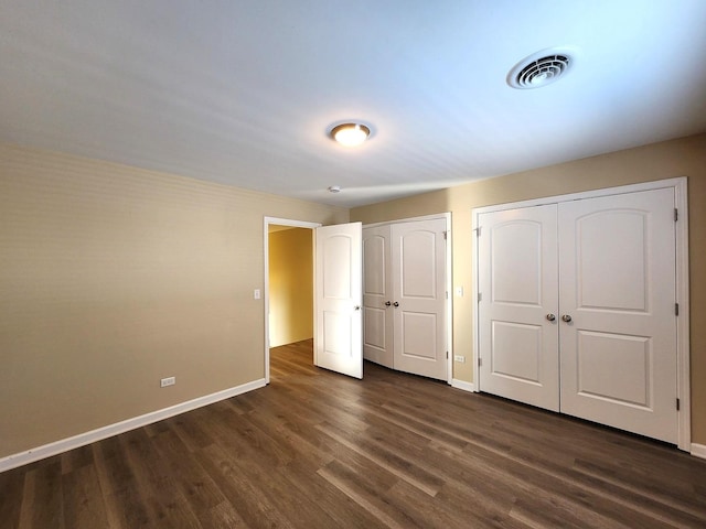 unfurnished bedroom featuring dark wood-type flooring, two closets, visible vents, and baseboards