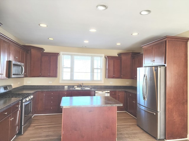 kitchen featuring dark wood finished floors, dark countertops, appliances with stainless steel finishes, a kitchen island, and a sink