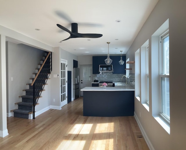 kitchen with light wood finished floors, light countertops, a peninsula, stainless steel appliances, and open shelves