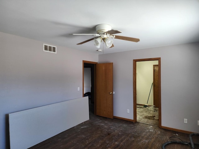 spare room with dark wood-type flooring, a ceiling fan, visible vents, and baseboards