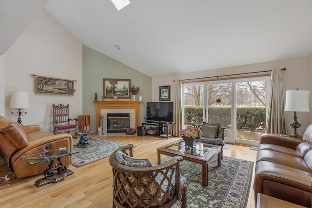 living room featuring hardwood / wood-style flooring, a fireplace, a skylight, and high vaulted ceiling