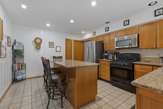 kitchen with a kitchen island, appliances with stainless steel finishes, a kitchen bar, light tile patterned floors, and light stone countertops