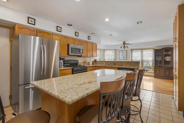 kitchen featuring light tile patterned floors, a breakfast bar, appliances with stainless steel finishes, a center island, and light stone counters