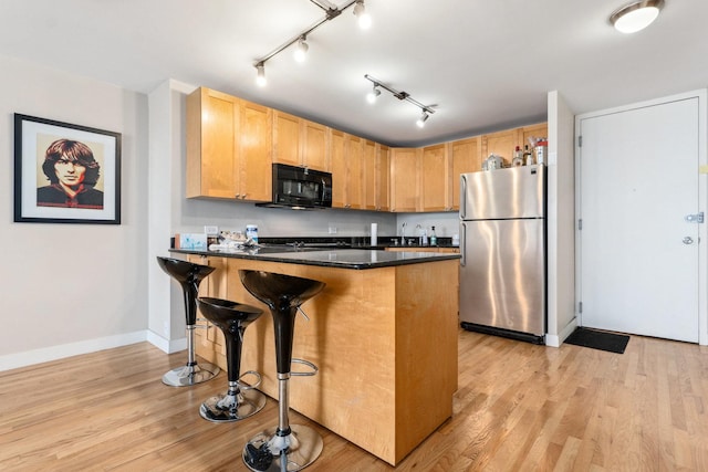 kitchen featuring a kitchen bar, stainless steel fridge, kitchen peninsula, and light hardwood / wood-style floors