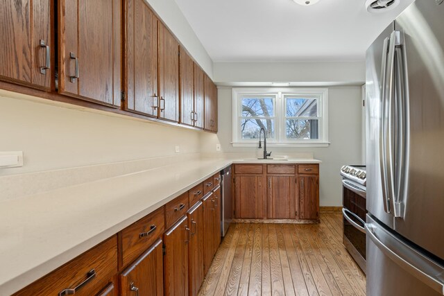 kitchen featuring light wood finished floors, brown cabinets, stainless steel appliances, light countertops, and a sink