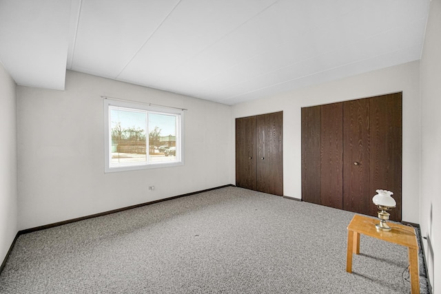 unfurnished bedroom featuring baseboards, carpet floors, and multiple closets